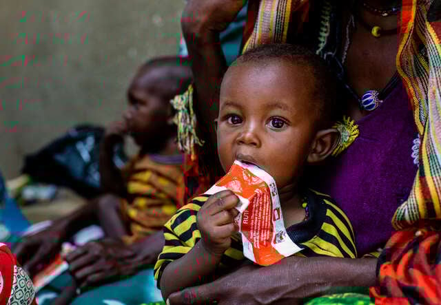 A child eating peanut paste and being help by his mother
