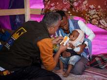 A 10-month old child is eating peanut paste while being tended to by an IRC nutrition officer in Yemen