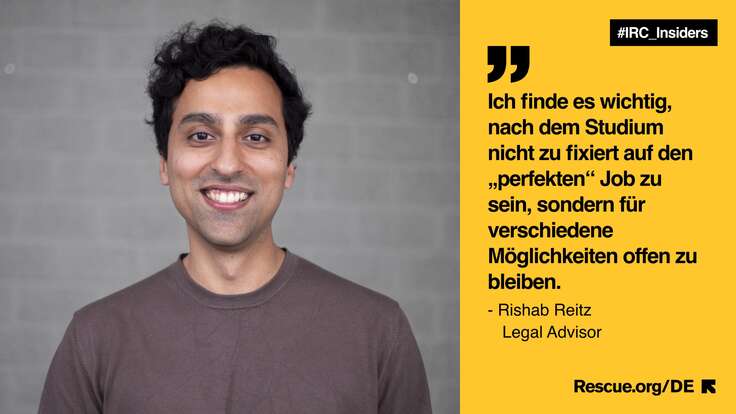 Ein Mann lächelt vor einer gelben Wand.