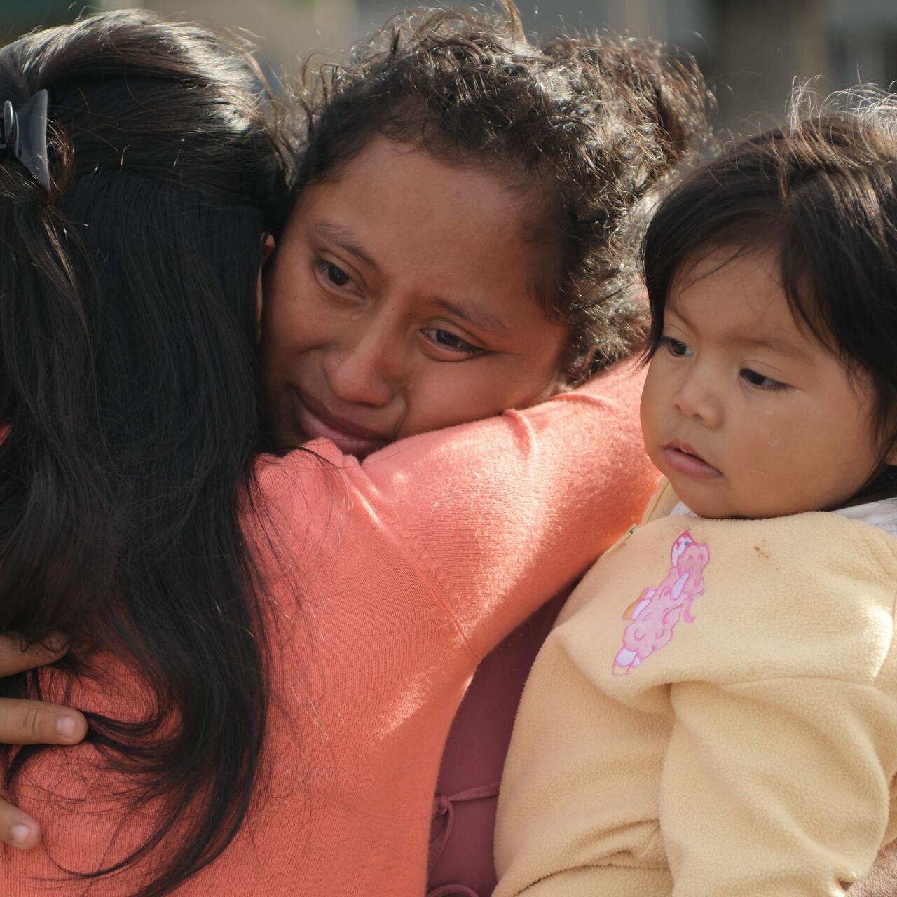 Eine Frau hält ein Kind im Arm, weint und umarmt eine andere Frau.