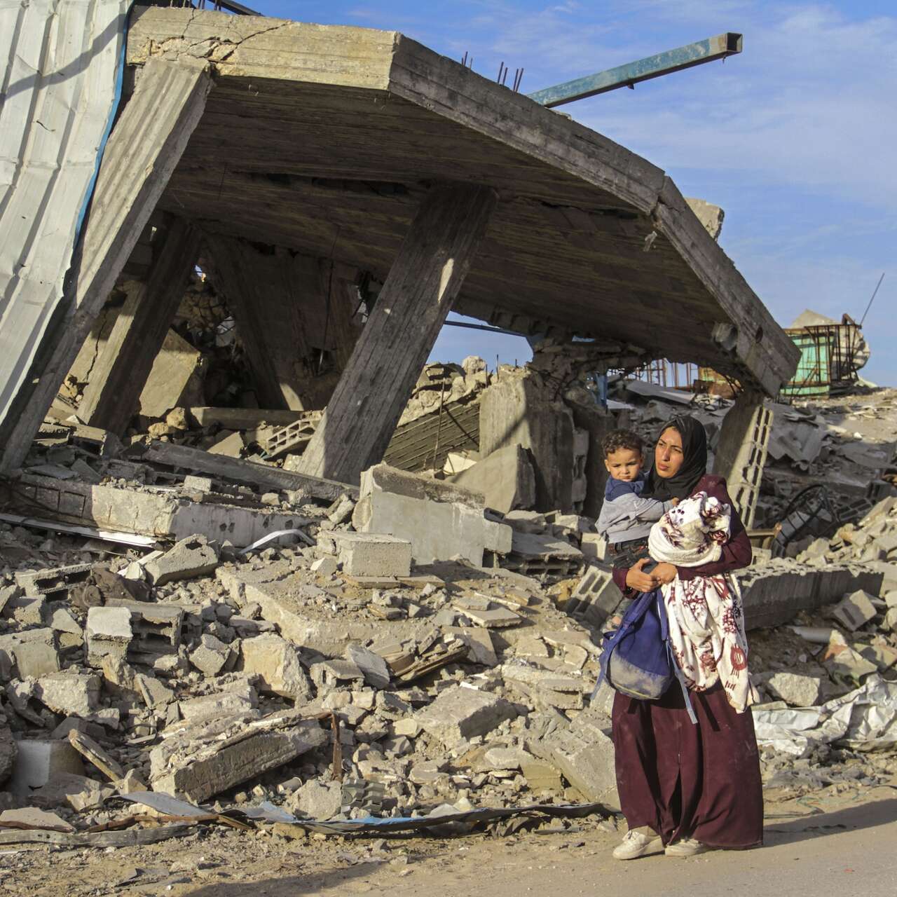 A woman holds a young child in her arms as she walks through a Palestinian community, destroyed by the war.