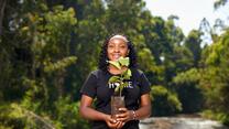 Elizabeth Wathuti looks at the camera and holds a vase with flowers outside in nature scenery