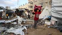 A boy carries a blanket through a destroyed neighborhood in Gaza.