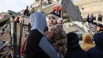 A young Palestinian child and their mother examine a destroyed building in their neighborhood
